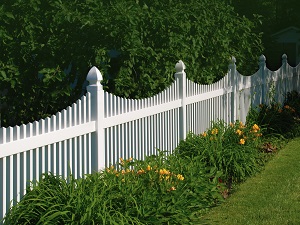 Showcase of white fence with gardening around it. 