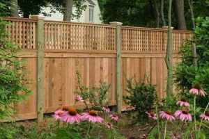Picture of a beautiful new wood fence with bushes and flowers in front of it.