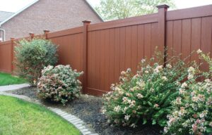A tall, wooden privacy fence with a garden of shrubs in front of it 