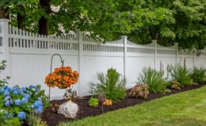Picture of a white fence behind landscaping in a backyard.
