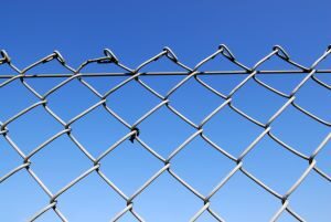 A close up of a chain-link fence with blue sky in the background.